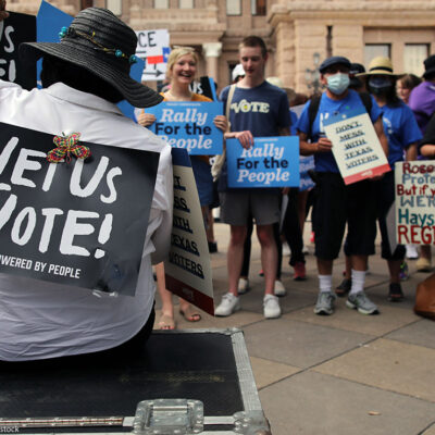 And group of demonstrators, one with a sign taped to their back saying "Let Us Vote!"