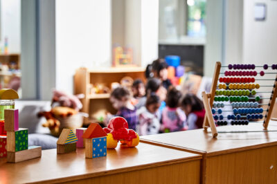 Toys in the forefront and preschoolers (blurred out) in class in the background.
