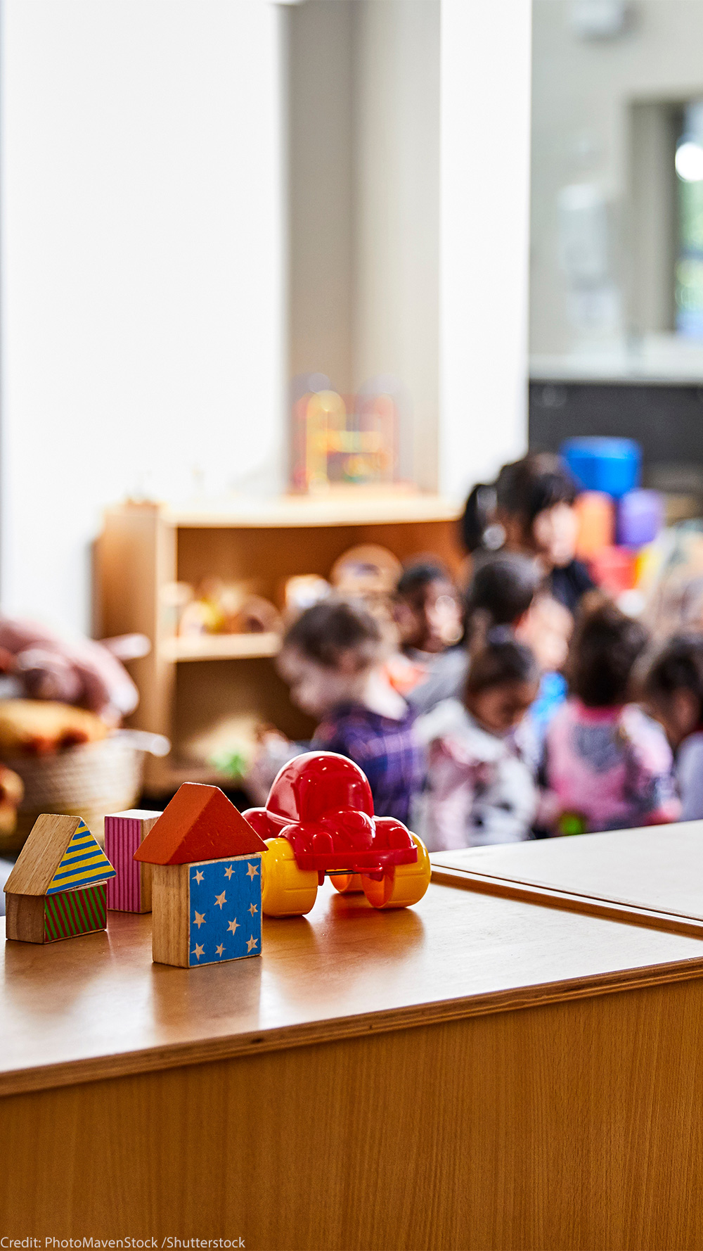Toys in the forefront and preschoolers (blurred out) in class in the background.