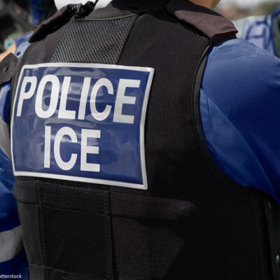 Close-up of POLICE ICE marking on the back of a vest uniform worn by a trio of officers.