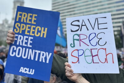 One protest sign reads: "Free Speech, Free Country." The other reads: "Save Free Speech"